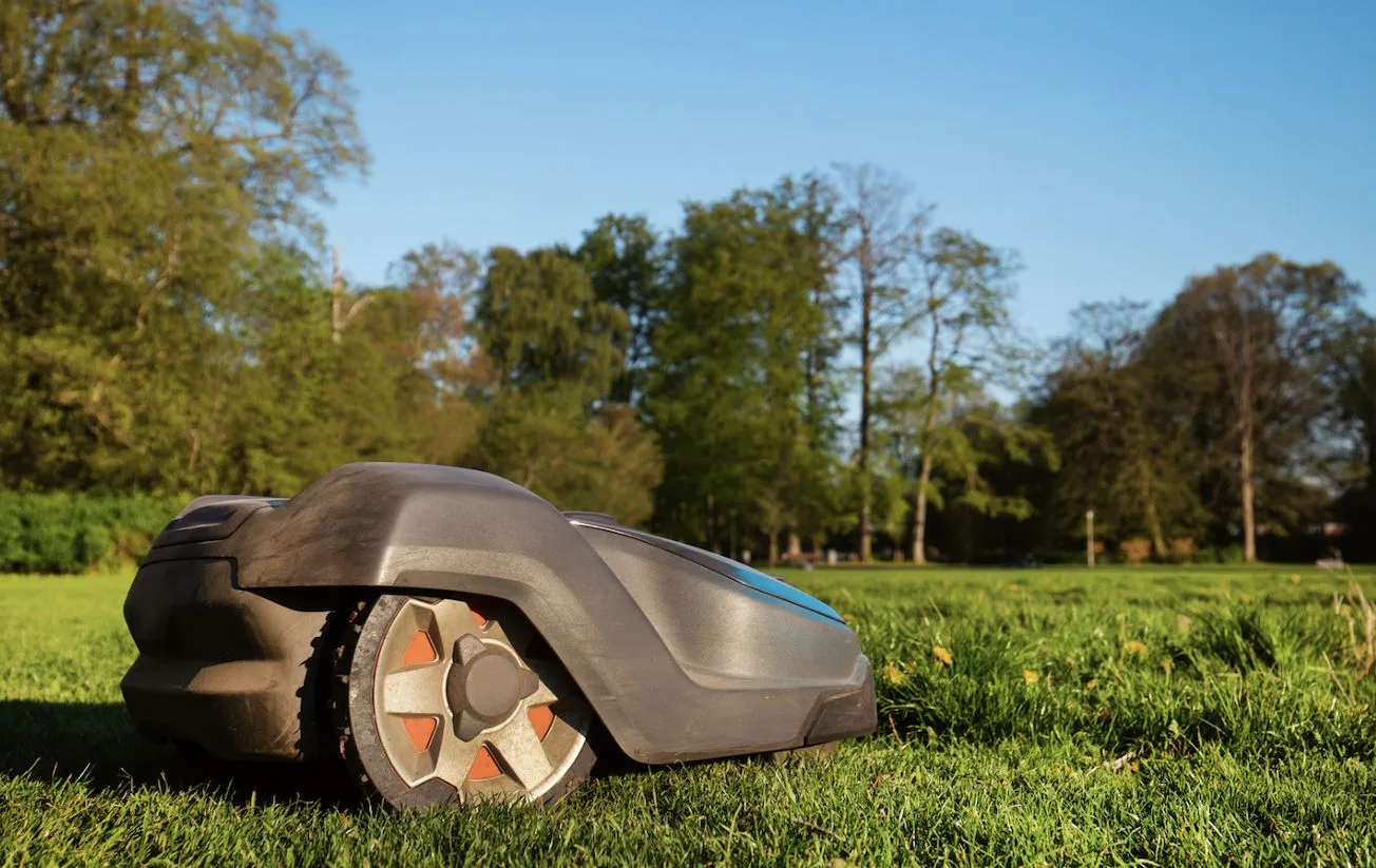 Mähroboter auf einer Wiese vor Bäumen Mähroboter auf einer Wiese vor Bäumen